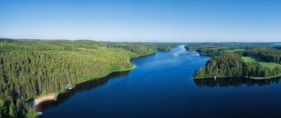 Aerial panorama of beautiful blue lake and green summer forest in Finland. Blue sky. Top view. Sunrise lanscape.