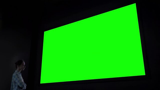 Green screen, technology, chroma key, futuristic, template, mock up, entertainment concept. Woman looking at large wall blank interactive green display at science exhibition, museum or cinema