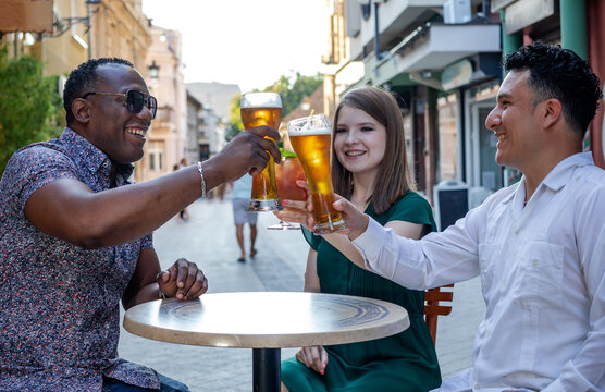 Multiracial group of friends drinking and toasting at street terrace of the cafe. Friendship concept with young multi ethnic people enjoying time together.