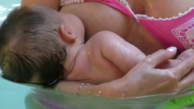 Young baby sucking milk from mother's breast in the pool