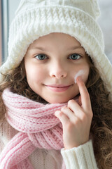 Cute little girl applying protecting cream to her face. Winter skin protection concept.