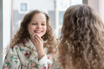 Portrait of beautiful little girl enjoying skincare procedures front of the mirror in her home bathroom.