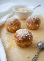 Freshly baked homemade brioche buns with pearl sugar on a baking paper with a spoon on the side and with a white napkin on a kitchen's table - food and drink.