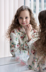 Fototapeta na wymiar Portrait of beautiful little girl enjoying skincare cleansing procedures front of the mirror in her home bathroom.