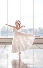 Cute little ballerina in white ballet costume and pointe shoes with is dancing in the room.