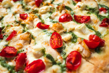 Closeup Delicious Italian pizza with tomatoes cherry, cheese, chicken, mozzarella and sauce pesto.