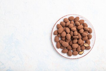 Almond in chocolate dragees on ceramic plate on white concrete background. Top view, copy space.