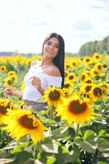 Obraz na płótnie Canvas Beautiful brunette woman in a white top on the field with sunflowers. Yellow sunflowers. Close plan.