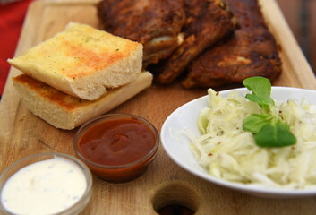 Knusprig gegrillte Spareribs mit Krautsalat, Dips und Baguette auf einem Holzbrett