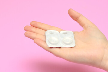 contact lenses in packaging on a woman's hands on a pink background