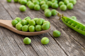 Fresh green peas with pod in wooden spoon on wooden table, healthy green vegetable or legume ( pisum sativum )