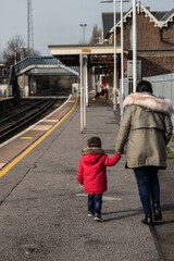 A mother and child holding hands on a train station platform