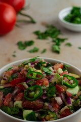 Kachumbari in a bowl with tomatoes and coriander in the background