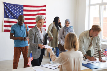 Multi-ethnic group of people registering at polling station decorated with American flags on...