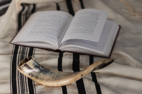 A shofar is placed on a tallit next to a Torah study book. Before the Jewish holidays of the month of Tishrei