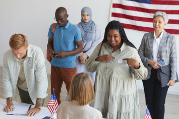 Multi-ethnic group of people registering at polling station decorated with American flags on...