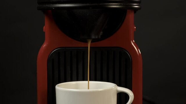 Close up of Red coffee machine making coffee on black background. When it finishes a hand enters and grabs the cup. 