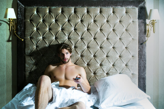 Carefree guy enjoying morning. Shirtless man in bedroom. Handsome man in underwear sitting on bed.