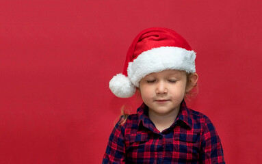 
little girl with closed eyes in red Santa hat on a red background. portrait. Merry Christmas and Happy Holidays.