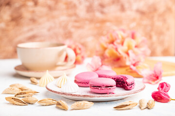Obraz na płótnie Canvas Purple macarons or macaroons cakes with cup of coffee on a white and brown concrete background. Side view, copy space, selective focus.