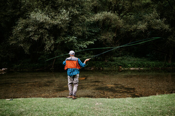 Senior man is fishing alone on fast mountain river. Active people and sport fly fishing concept.