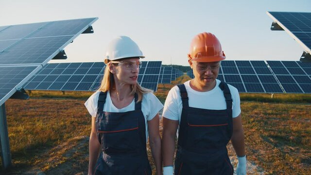 Happy couple of multi-race workers monitoring solar batteries system maintenance and talking friendly conversation. Solar park. Solar panels. Ecology concept.