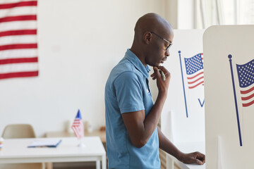 Side view portrait of young African-American man standing in voting booth and thinking, copy space