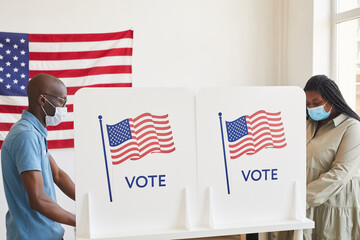 Side view portrait of two African-American people wearing masks standing in voting booths opposite...