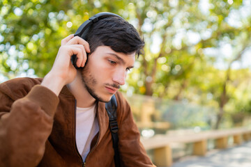 Young man listening music with headphones outdoors.