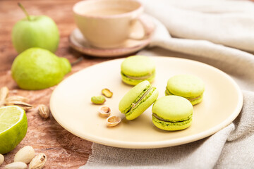 Green macarons or macaroons cakes with cup of coffee on a brown concrete background. Side view, selective focus.