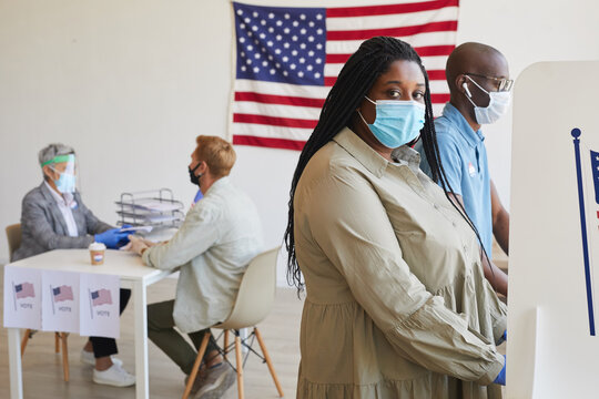 Side view portrait of female African-American voter standing in booth and looking at camera on post-pandemic election day, copy space