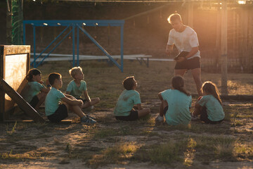 Male fitness coach giving instructions to the kids at a bootcamp