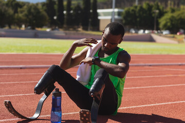Black African American Male athlete with prosthetic leg sitting on race track