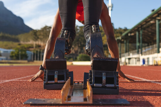 Rear view of Black African American male athlete with prosthetic leg bending on starting blocks