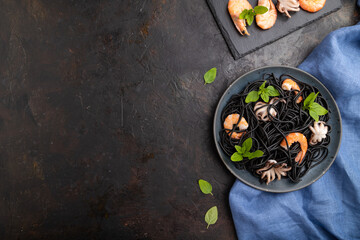 Black cuttlefish ink pasta with shrimps or prawns and small octopuses on gray wooden background. Top view, copy space.