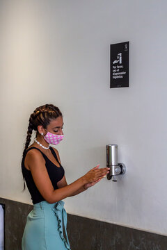 Mujer joven con mascarilla lavándose las manos con gel hidroalcohólico cumpliendo las medidas de seguridad y distanciamiento social de la pandemia COVID-19 en baño publico