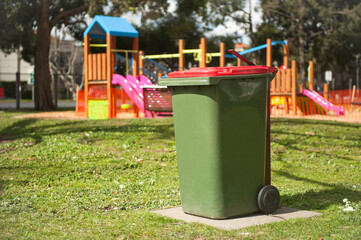 Recycling bin stands outdoor near playground. Australia, Melbourne. Green bin. 