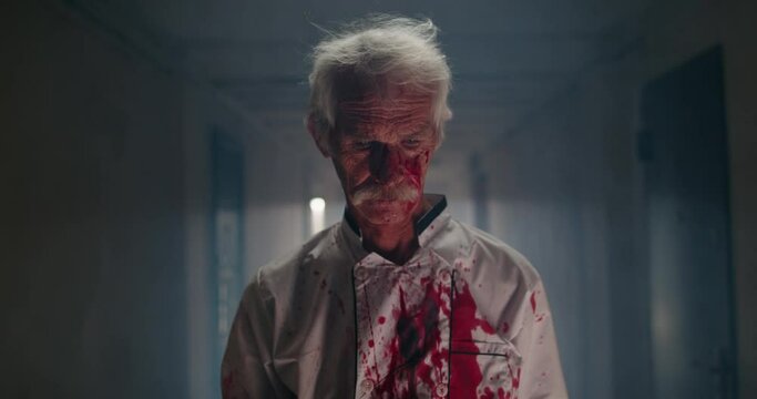 Creepy senior mustached maniac in hallway. Bloodlust butcher covered in blood carrying an axe, dressed for a halloween thematic party 4k footage