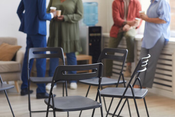 Cropped shot of empty chairs in circle during support group meeting with people chatting in...