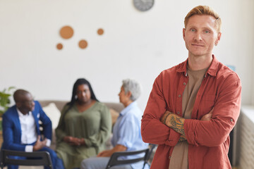 Waist up portrait of modern tattooed man posing confidently and looking at camera with people...