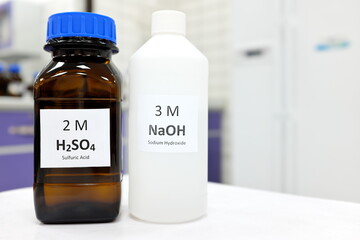 Selective focus of sodium hydroxide base and sulfuric acid solution in brown glass and plastic bottle inside a chemistry laboratory. White background with copy space.