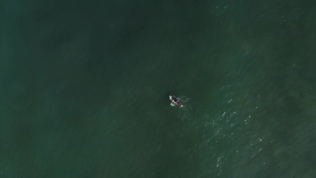 Aerial: top down view of surfer paddling out to waves and jumping off surfboard