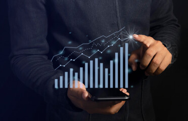 ฺBusiness man holds a mobile phone and displays a holographic graph showing statistics of profitable graphs, ideas of growth planning and business strategies to see trends in good business.