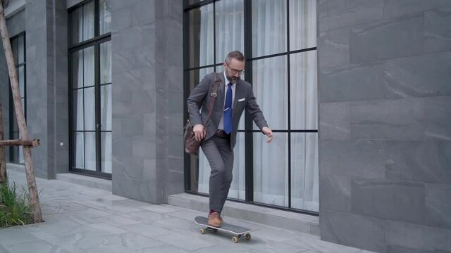 Slow motion of Confidence Caucasian business man office worker in suit carrying briefcase with skateboarding on office district. Handsome beard guy businessman entrepreneur riding skateboard in city.
