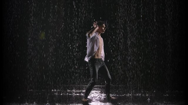 Modern ballet, a man performs elements of modern choreography while standing on the surface of the water in the rain. Slow motion.
