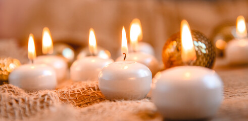 Obraz na płótnie Canvas Lit candles, Christmas tree Golden baubles and burlap on a wooden background. New year's and Christmas concept