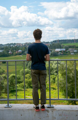 The young man stands at the railing with his back to the camera.