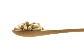 Herbal medicine in capsules on wooden spoon.