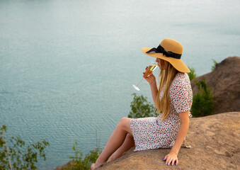 A girl sits with a glass of champagne on a hill.