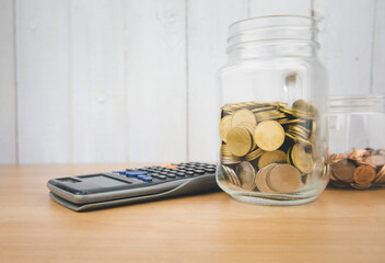 A pile of coins in a glass jar with a calculator beside Financial concepts.